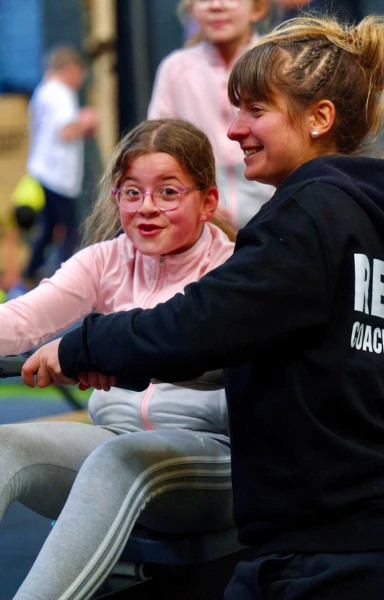 Séance CrossFit Kids à CrossFit RENGŌ Valenciennes, une coach accompagne une jeune fille sur rameur dans un environnement bienveillant et ludique.